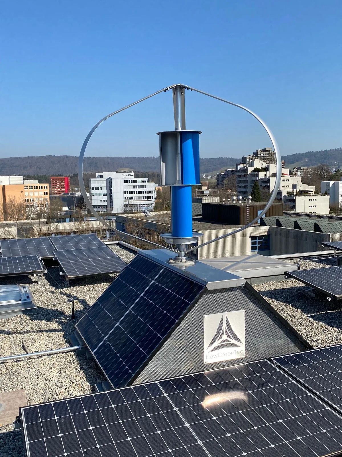Die New Green Tec Int. AG aus Dübendorf kombiniert Windturbinen mit Solarpanels. Ein Hausdach mit Solarpanels und einer vertikal drehenden Windturbine.